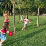 Kids and adults enjoy playing together in a lush, sunny park setting.